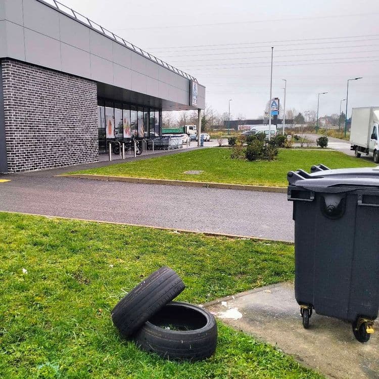 Pneus usagés abandonnés à côté de poubelles d'un supermarché 